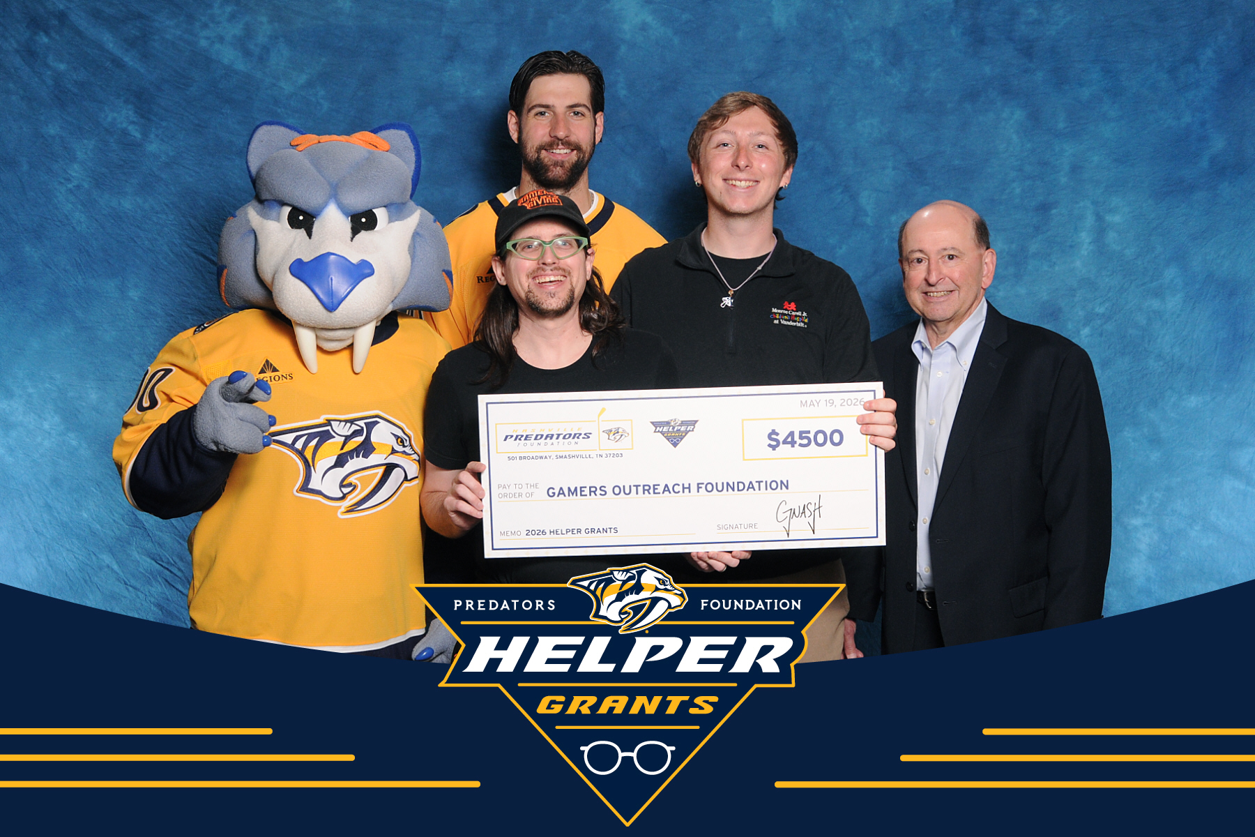 A photograph of Joe Hills and Vanderbilt Children's hospital technologist Graden Knapp receiving a Predators Foundation Helper Grant check from Gnash, Gerry Helper, and Nicholas Hague. The check is for $4500 with the memo line "2026 Helper Grants"