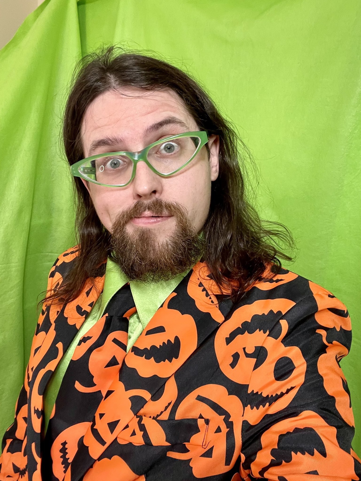 A photograph of Joe Hills with combed hair wearing a pumpkin jacket with matching tie over a button-down green silk shirt 